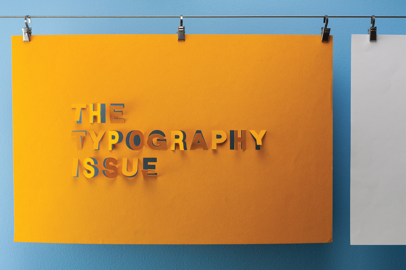 The Typography Issue letters cut out of a sheet of orange paper hanging on a line